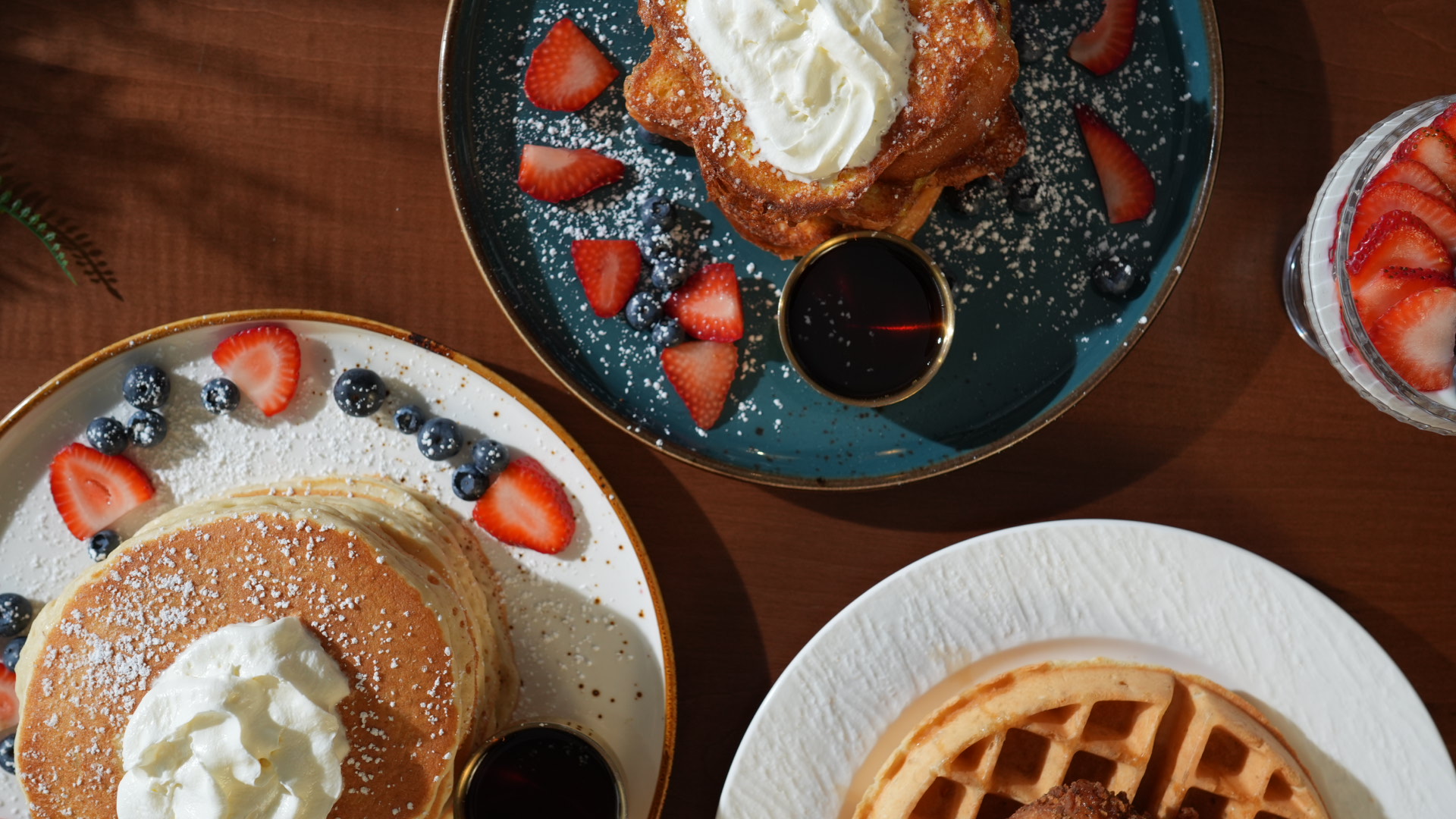 Overhead flatlay of pancakes, French toast, Belgian waffles and a strawberry parfait with maple syrup at SOLENA