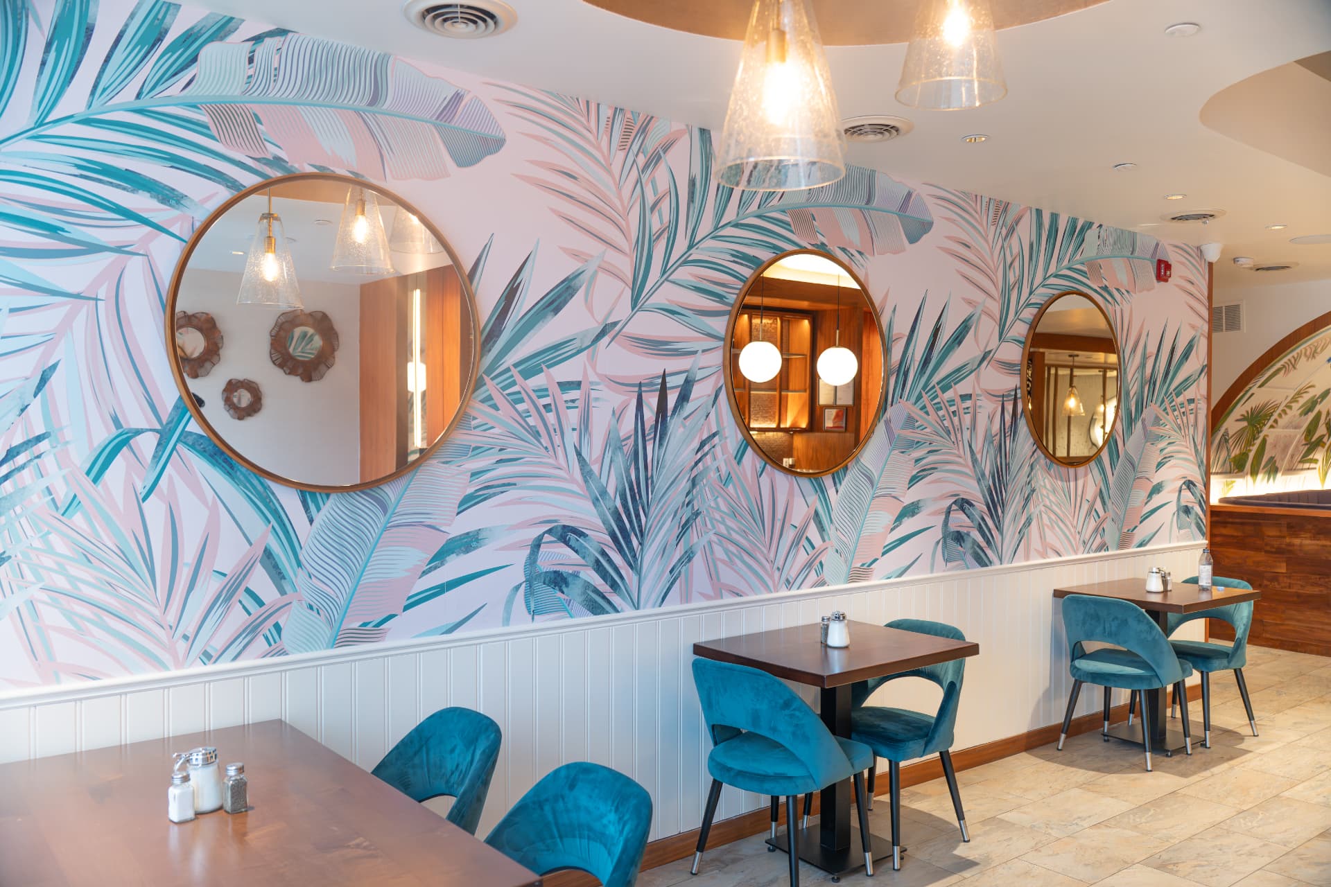 SOLENA Brunch & Bar dining room in Corso Italia, Toronto — pastel palm mural, round brass mirrors and teal velvet chairs