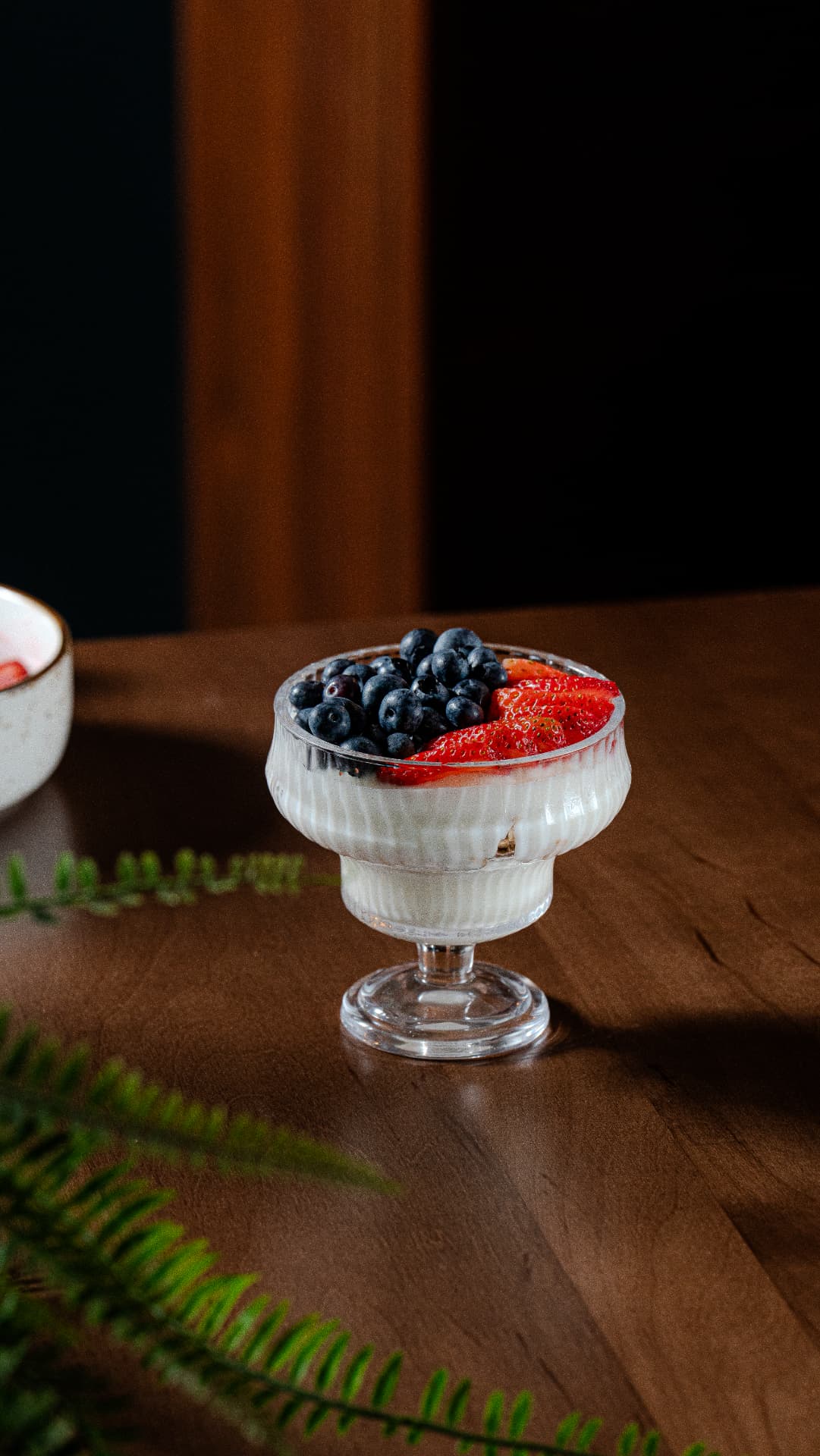 Berry yogurt parfait in a fluted glass with blueberries and strawberries on a walnut table at SOLENA
