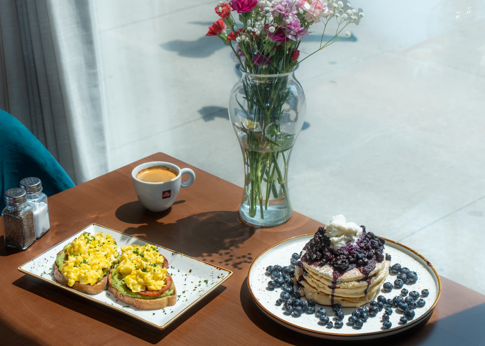 Window table at SOLENA set with avocado toast, blueberry pancakes, espresso and fresh flowers