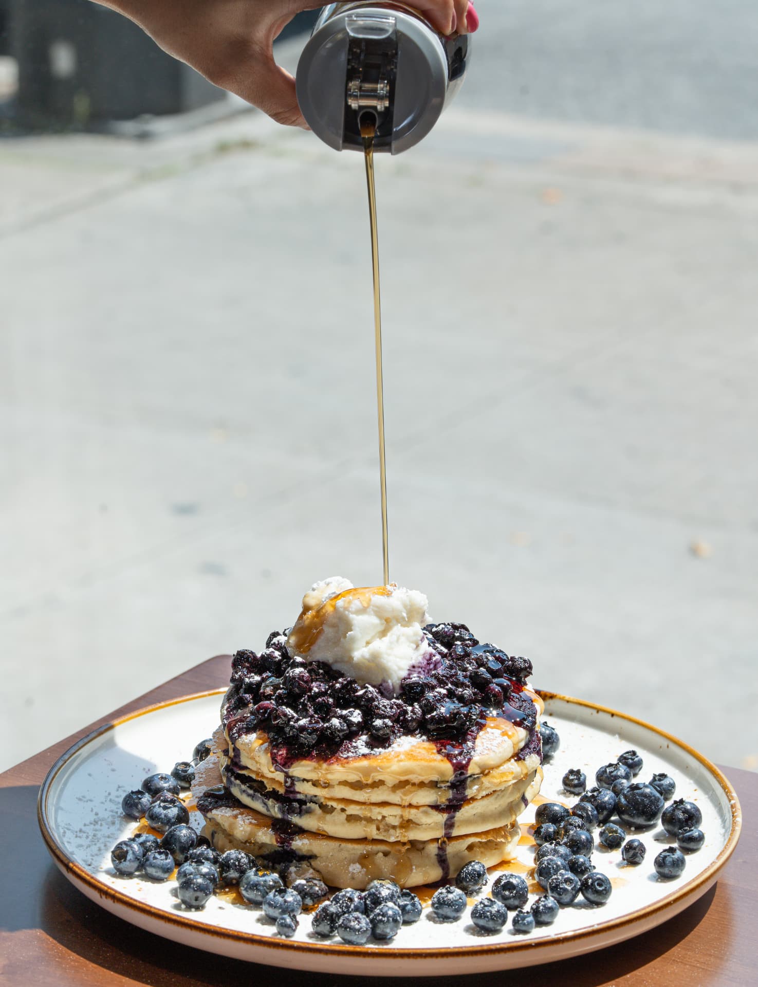 Blueberry pancakes with whipped ricotta and fresh blueberries, maple syrup being poured on the patio at SOLENA