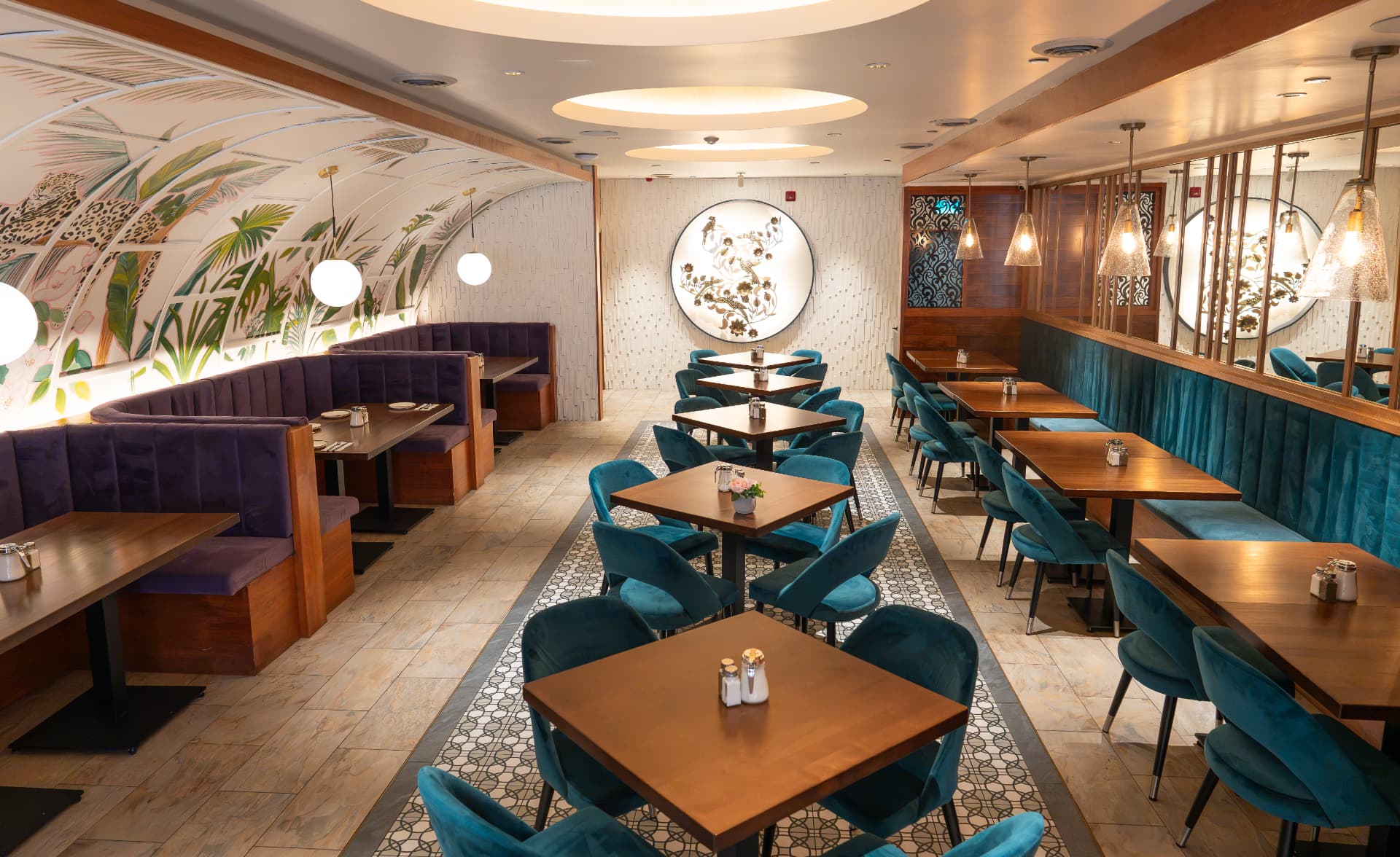 View down the SOLENA dining room aisle with patterned tile, brass wall art and velvet seating