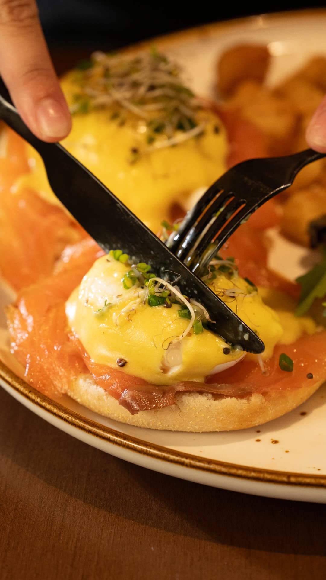Knife and fork cutting into a poached egg on smoked salmon benedict with hollandaise at SOLENA