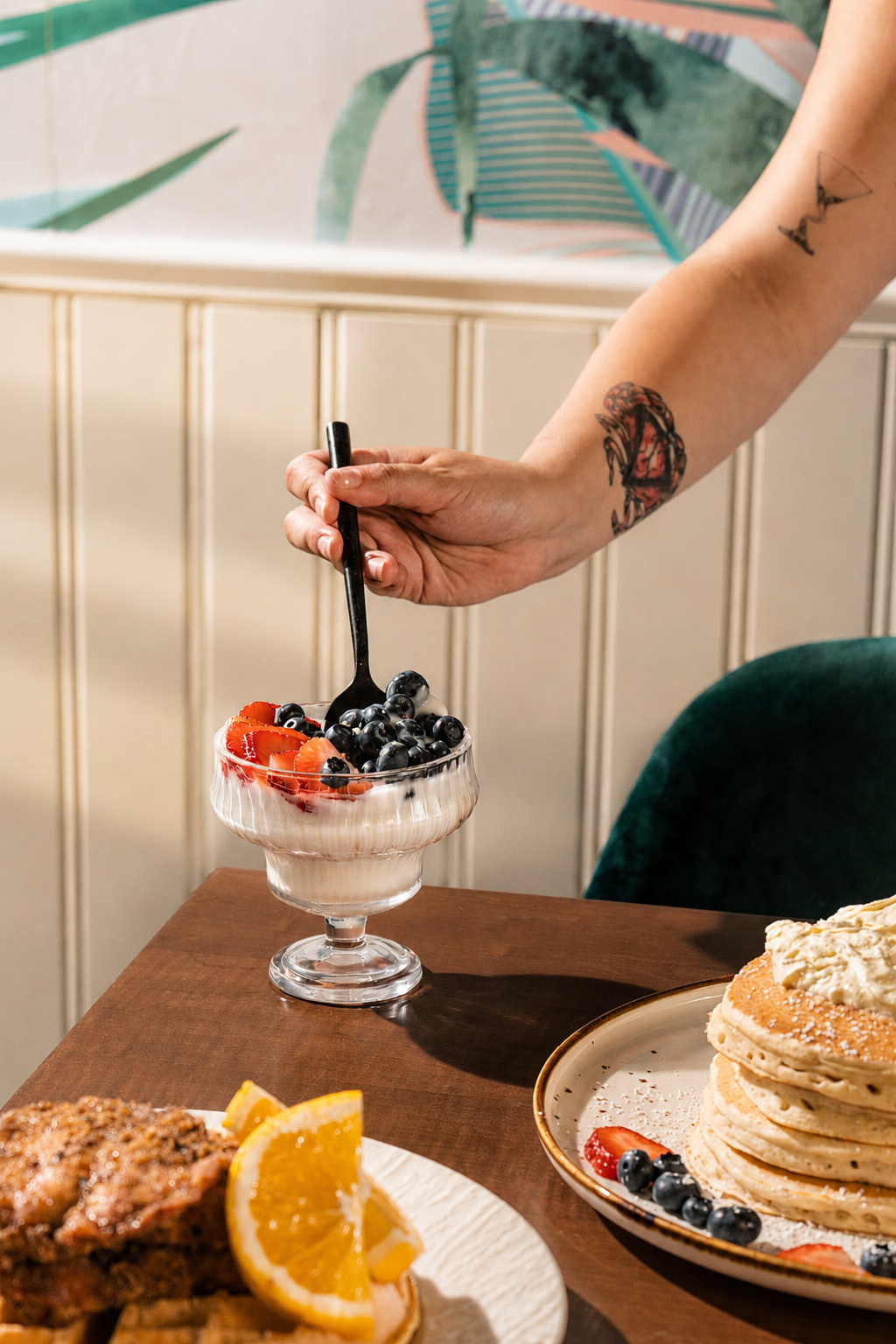 Berry yogurt parfait being served in a fluted glass beside pancakes and waffles at SOLENA