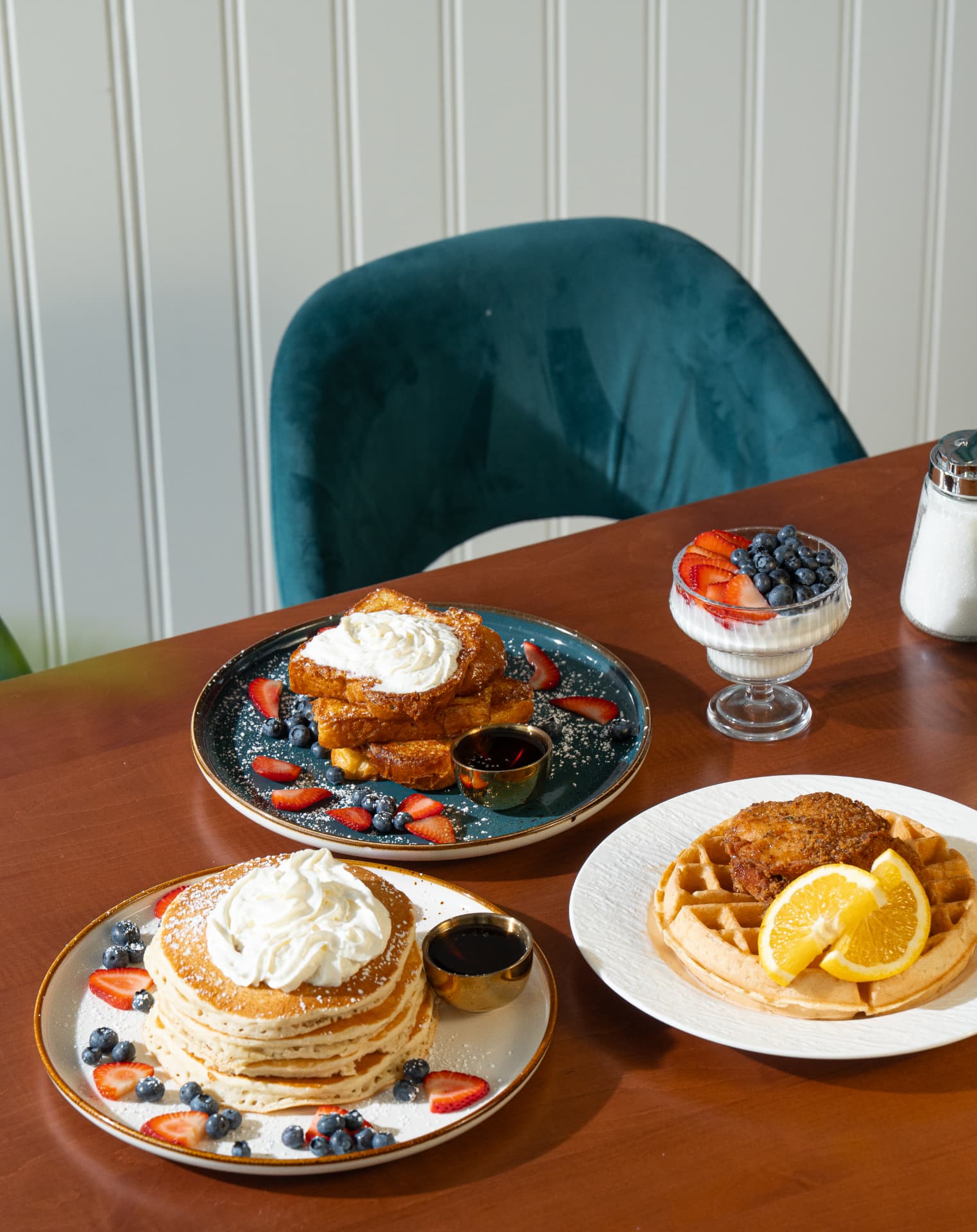 French toast, pancake stack, chicken and waffles and a berry parfait on a walnut table at SOLENA