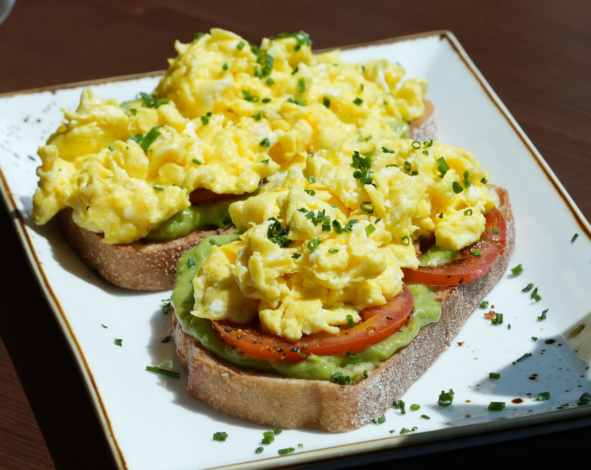 Two slices of avocado toast with soft scrambled eggs, tomato and chives at SOLENA