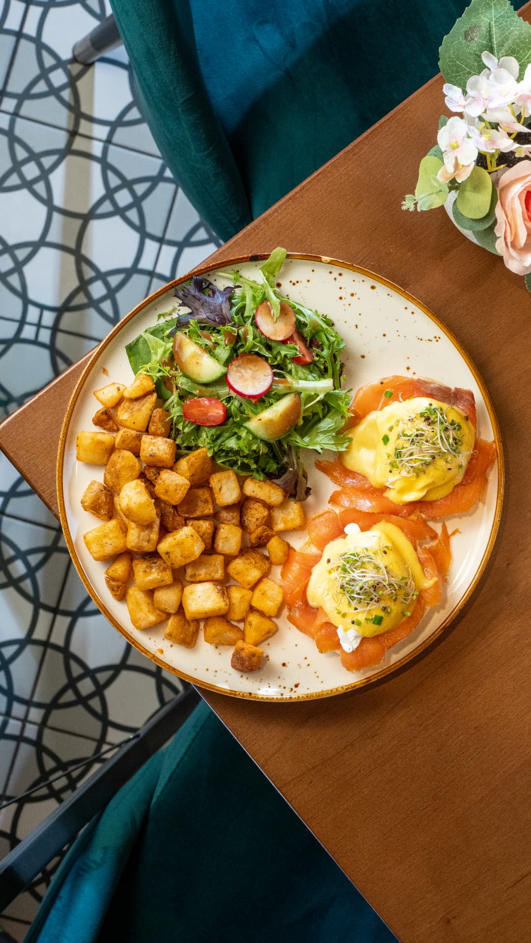 Top-down view of smoked salmon benedict with home fries and mixed greens on a wooden table at SOLENA