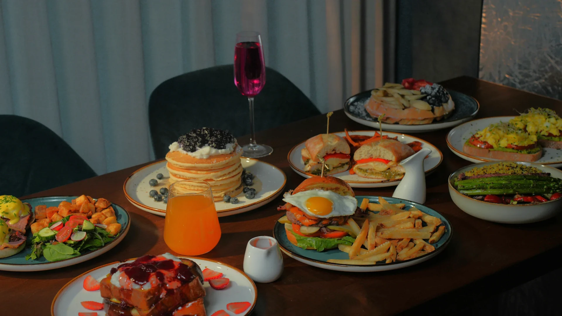 A Solena table spread — pancakes, benedicts, burgers, waffles, and a berry mimosa