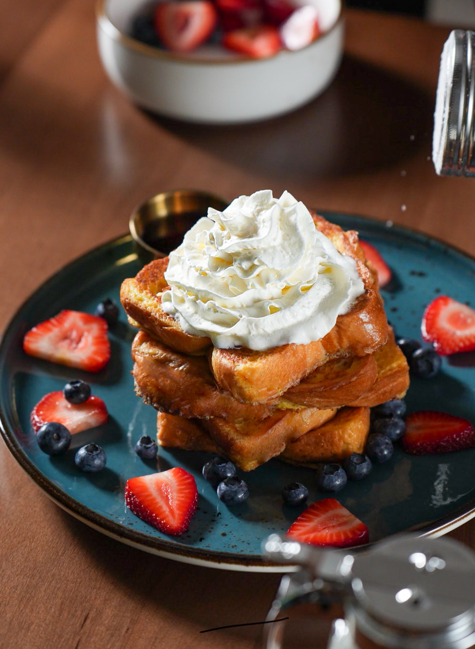 Brioche French toast stacked with whipped cream, strawberries and blueberries on a teal plate at SOLENA