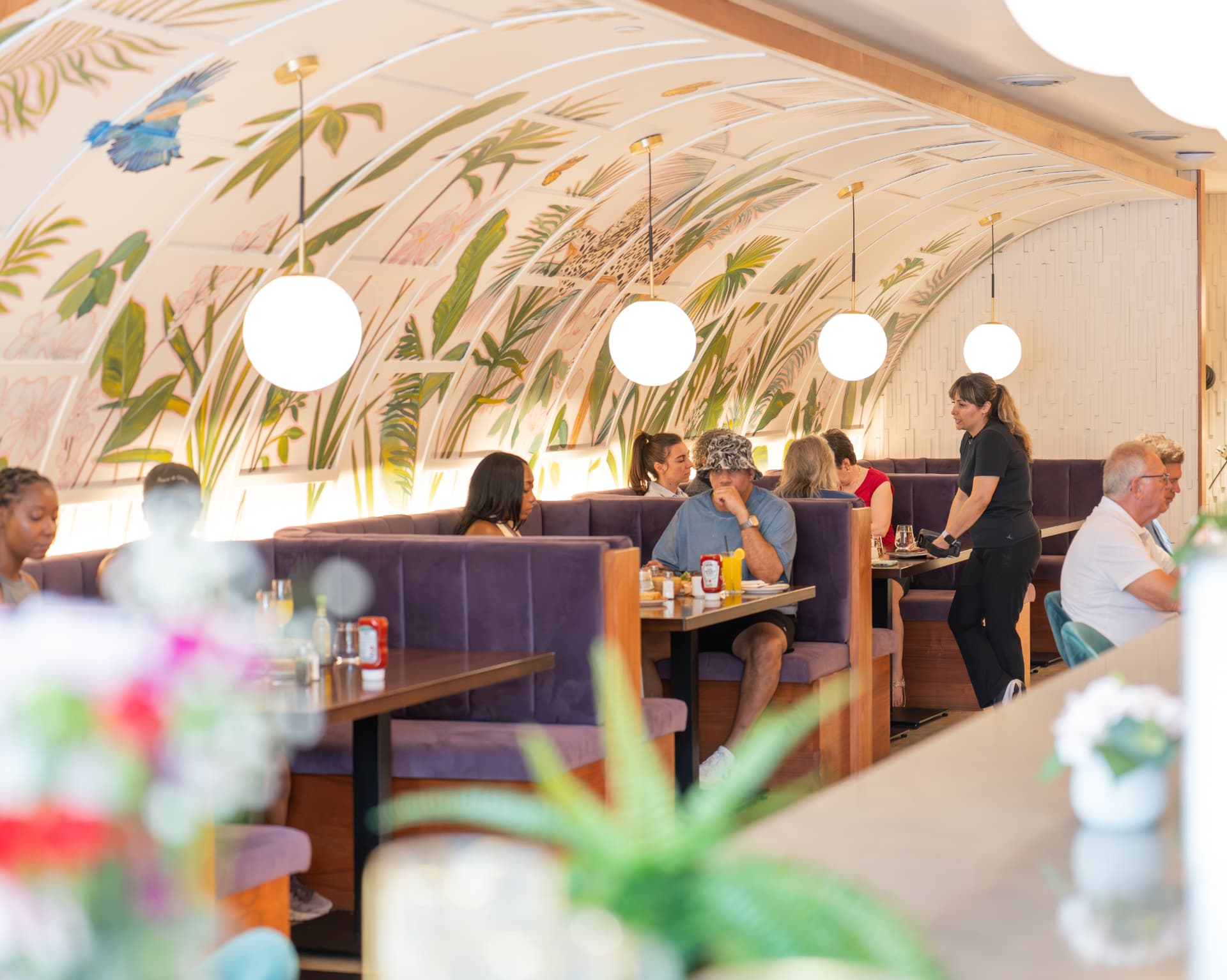 Guests enjoying brunch in SOLENA's mural-lined booths under globe pendant lights
