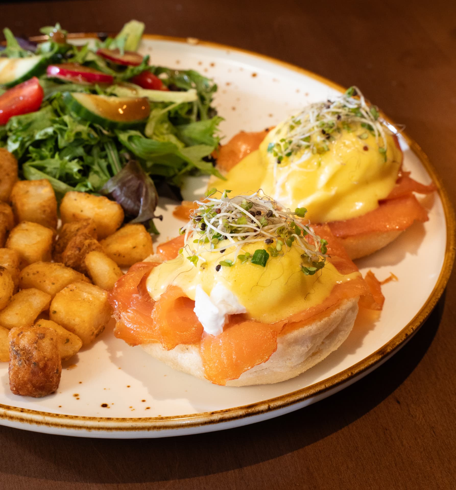 Smoked salmon benedict topped with sprouts and hollandaise, served with crispy potato cubes and salad at SOLENA
